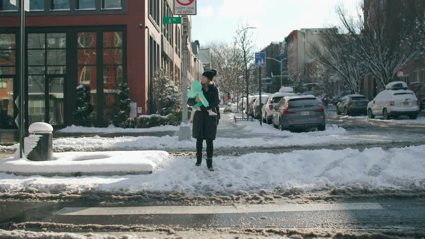 Mother holding a baby crosses the road over the snow in the city at morning