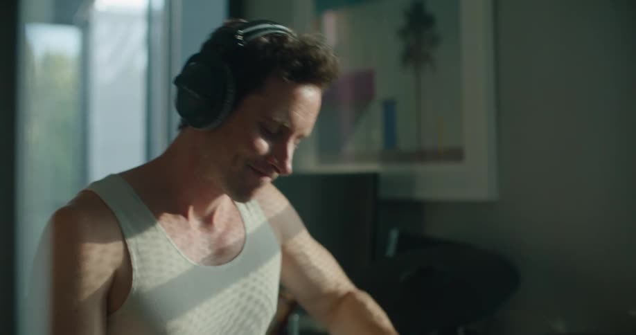 Frustrated young man wearing headphones playing drums in the living room at home in the morning