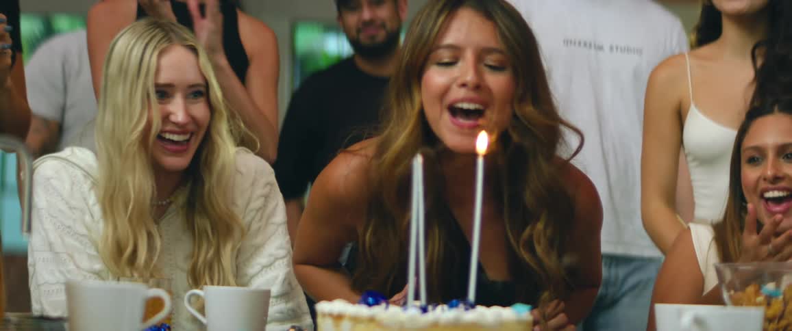 Young pretty female blowing out long tapered candles on a cake surrounded by friends