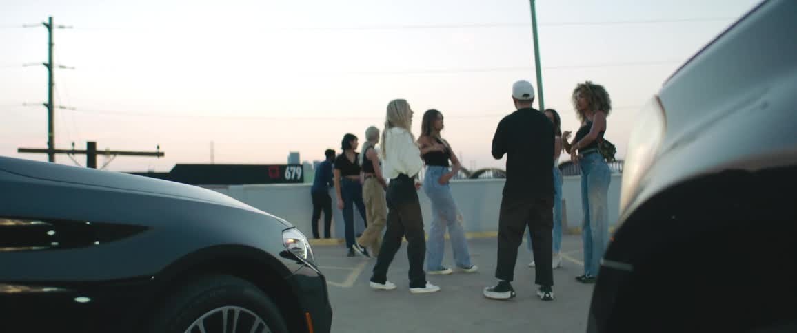 Group of friends talking on a parking lot in front of cars at sunset
