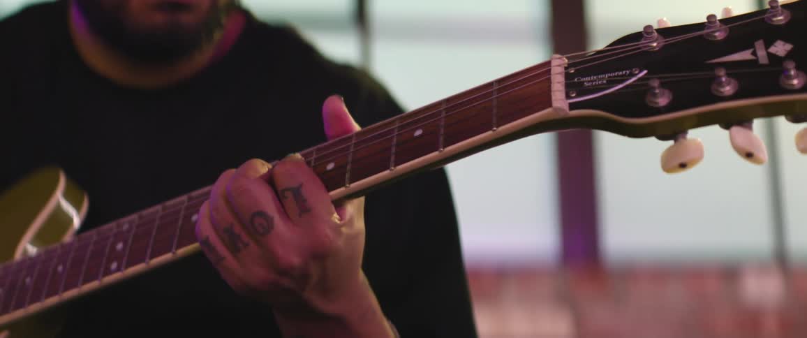 Bearded man wearing a baseball cap plays the guitar inside a room