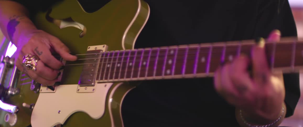 Male guitarist with tattoos wearing jewelry plays electric guitar