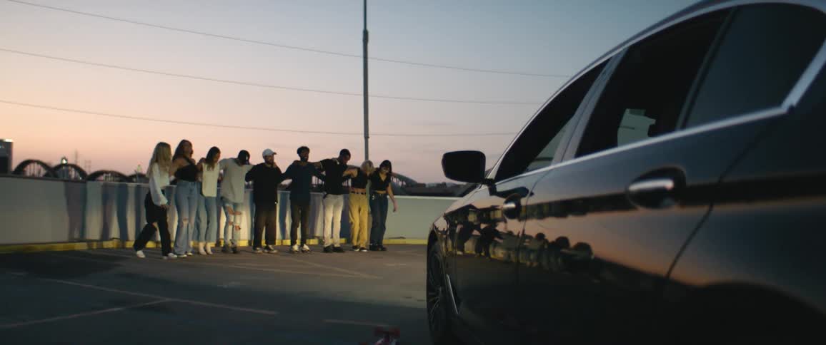 Group of men and women stand in a semi circle with their arms interlocked and move out into a straight line