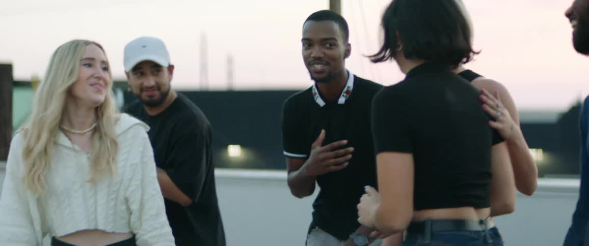A group of friends with black and white shirts and pants dances on rooftop at dusk