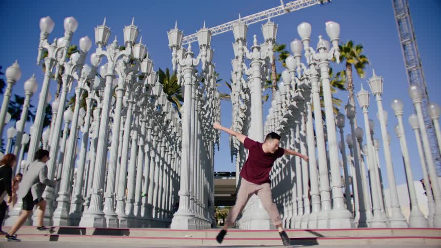 A man dances hip hop style in front of a public art display