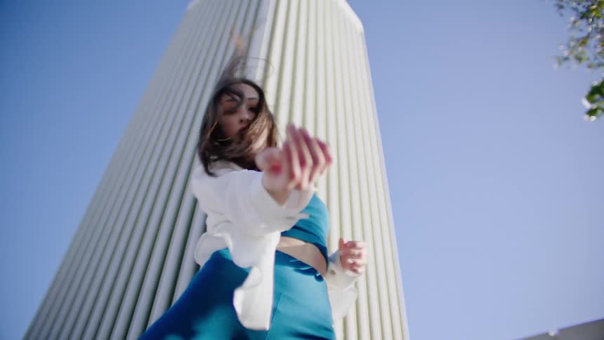 Young woman energetically dancing in front of a white skyscraper in the city