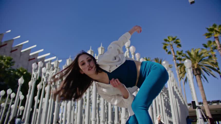 Young woman energetically dancing in front of streetlamps on a park in the city