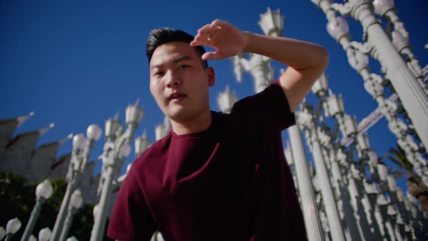 Young asian man energetically dancing in front of a streetlamps on a park under a blue sky