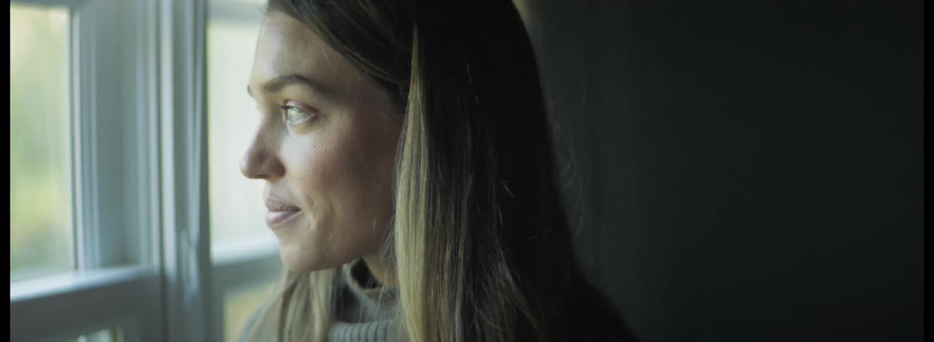 Close up of the face of a woman standing in a room looking out a window