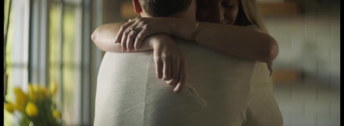 Man and woman embrace and hug each other as the woman holds a pregnancy test device