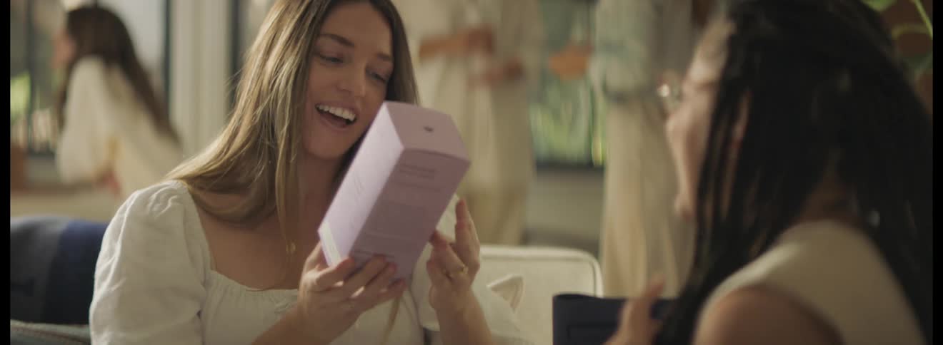 Woman sitting on a couch at a party receives a gift from a friend