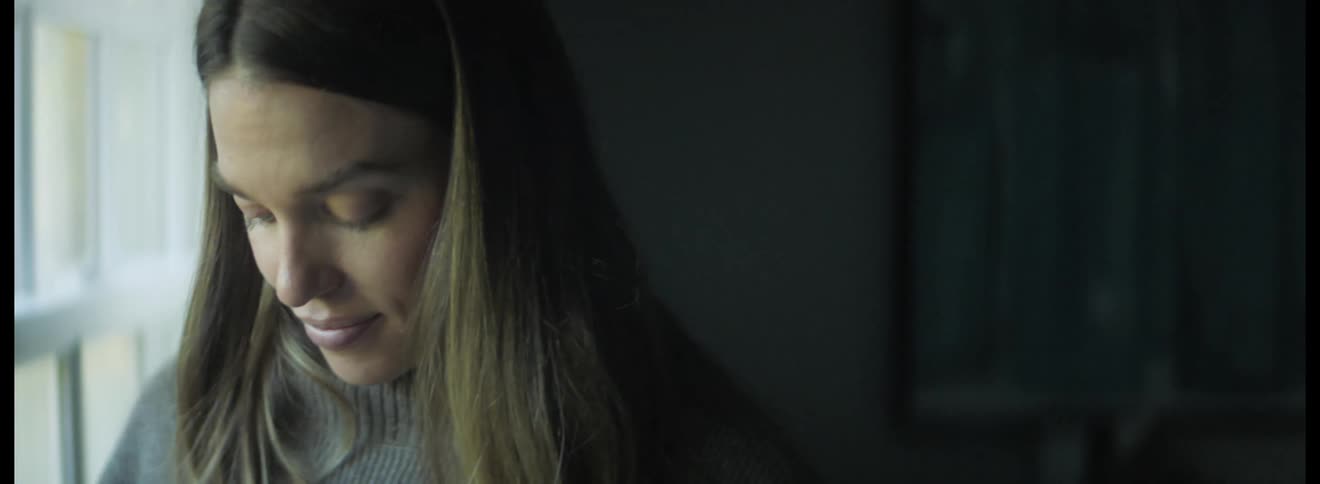 Woman wearing a grey sweater standing next to the window touching her pregnant belly
