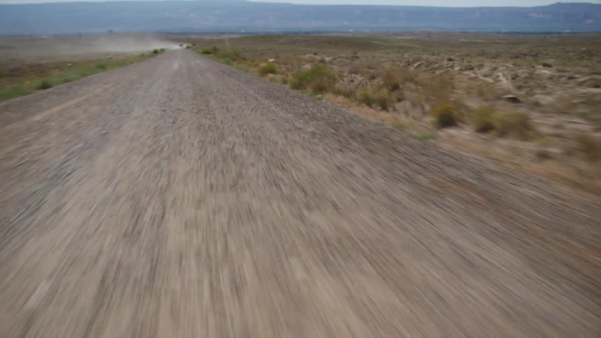Vehicle drives on country road with distant mesa in the background in the plains