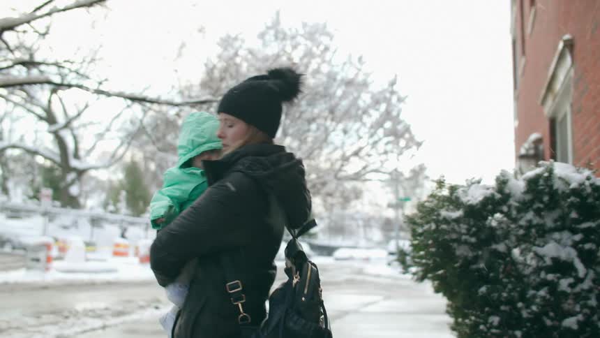 A mother picks up her baby and walks on the sidewalk