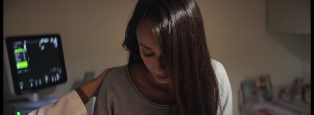 Woman wipes her tears with a tissue then a doctor touches her shoulder to console her while in the doctors office