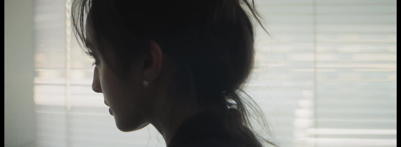 Woman with her hair up and wearing an earring blinks her eyes as she stands in front of a mirror