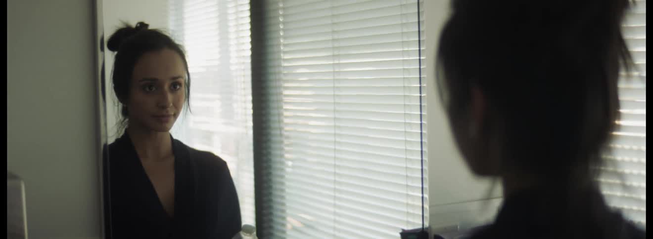 A woman takes deep breaths as she looks at her reflection in an office bathroom