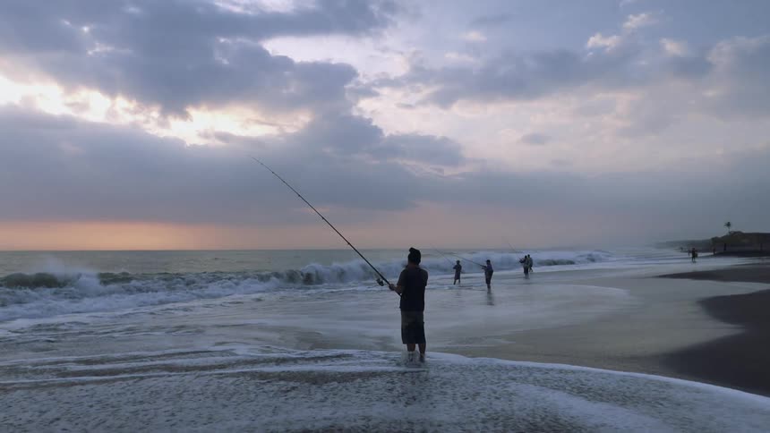 Men standing in front of the ocean and fishing at a public beach