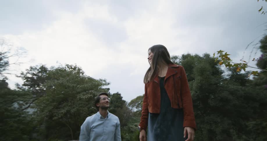 A man walks beside his girlfriend as she uses tree stumps as a balance beam