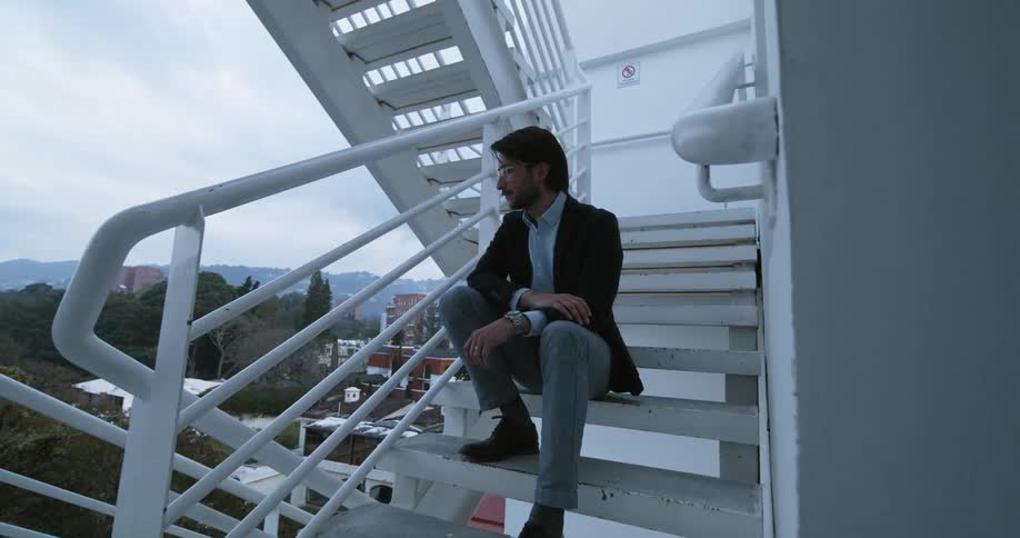 A man sits on steps outside a building and looks toward the city