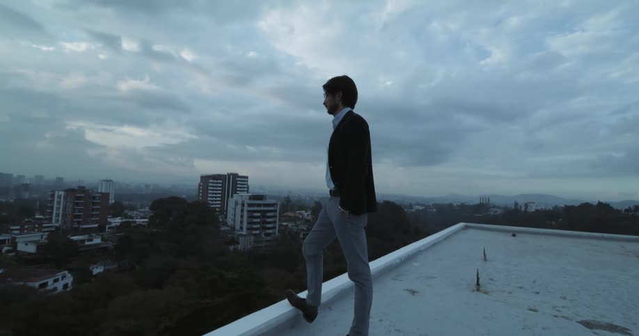 Man wearing formal clothes standing on the edge of a buildings rooftop looking to the city ahead