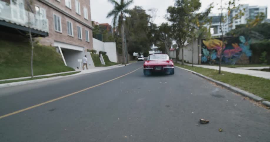 Red vintage corvette backing down the street from a neighborhood