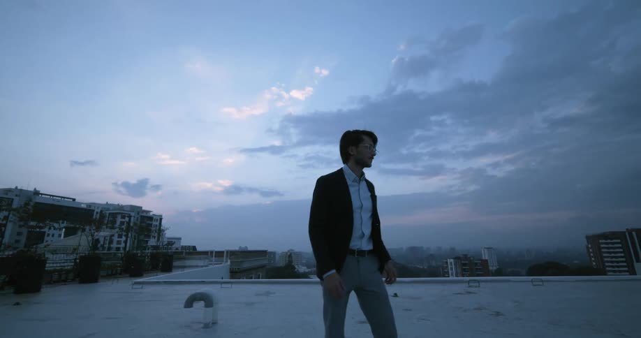 Man wearing formal clothes walking on a building rooftop in the middle of a big city on a cloudy day
