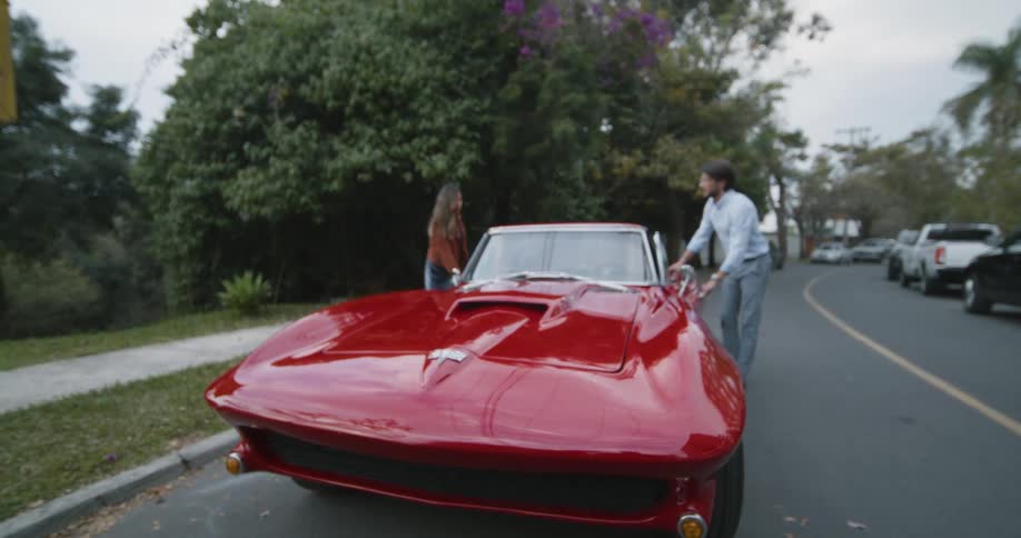 Couple walk and enters a bright red sports car parked on the street