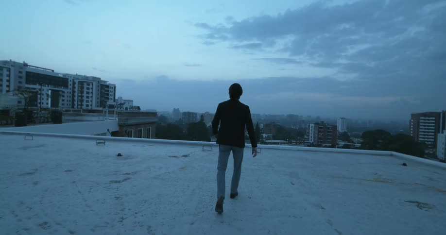 A man throws his arms up while posing and turns to walk across the rooftop of a downtown building