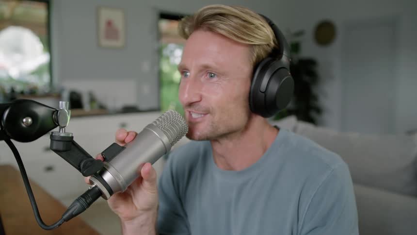 Radio host wearing a headphone inside his house talking to a radio microphone