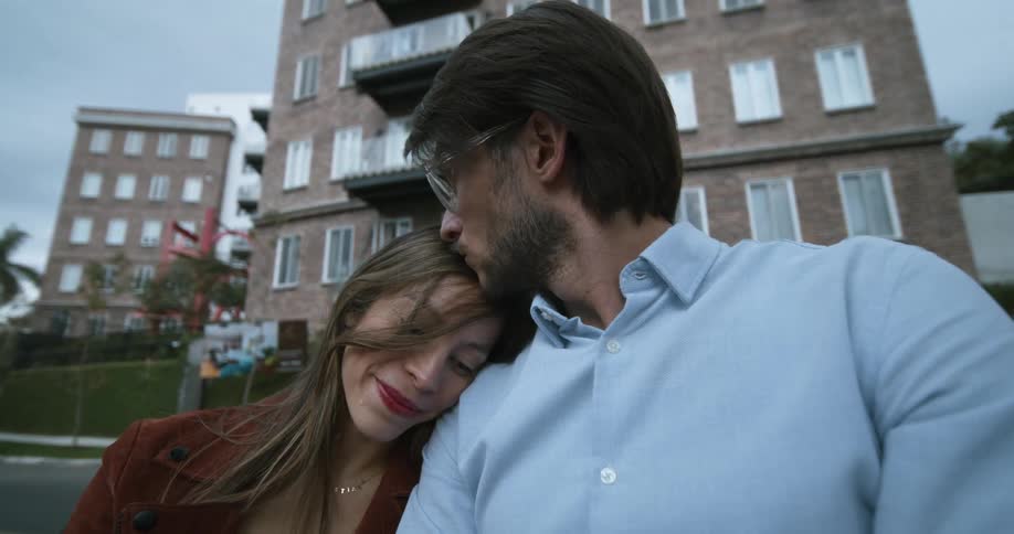 Man kissing the head of a woman while sitting together outdoors in a public street