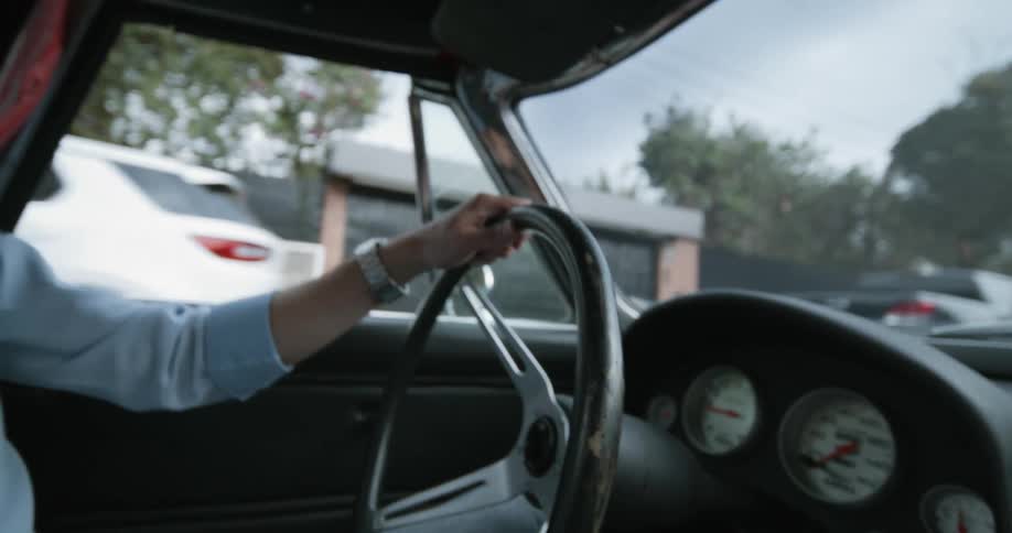 Hand of a man driving a vintage car down a residential street