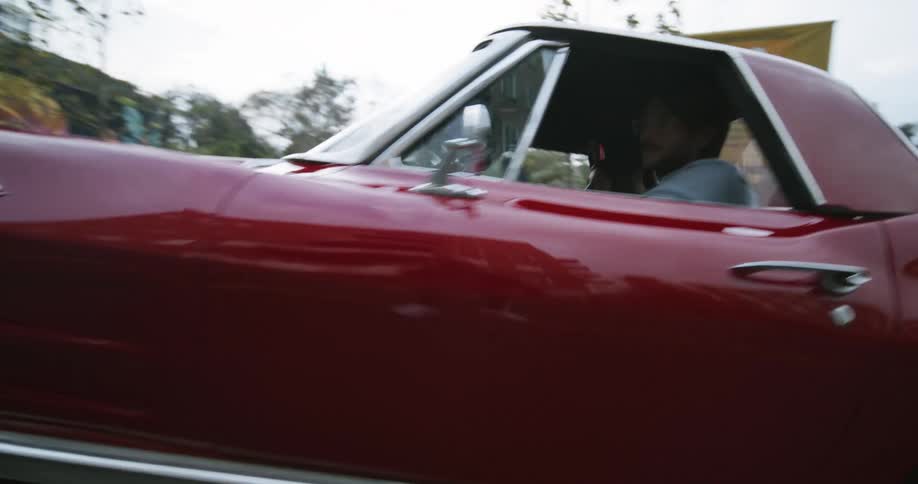 A man in a bright red classic sports car gradually accelerates along a paved road