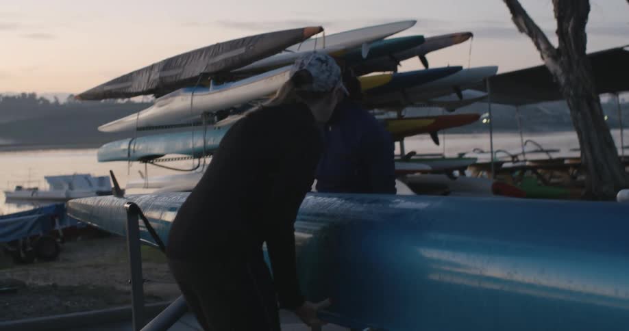 Two women set a boat down on a stand on the shore
