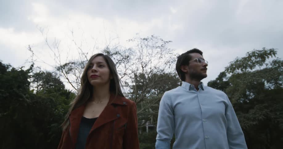 Man and woman walking along a street with trees on the sides and a house at the background