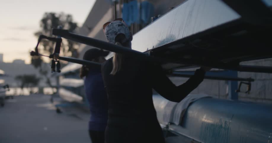 Two women lift a row boat off the rack