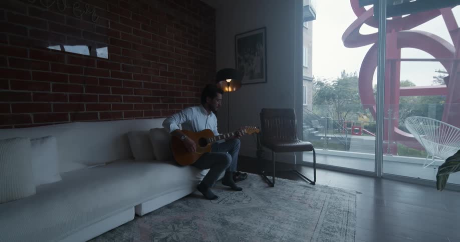 A man is playing guitar on his couch
