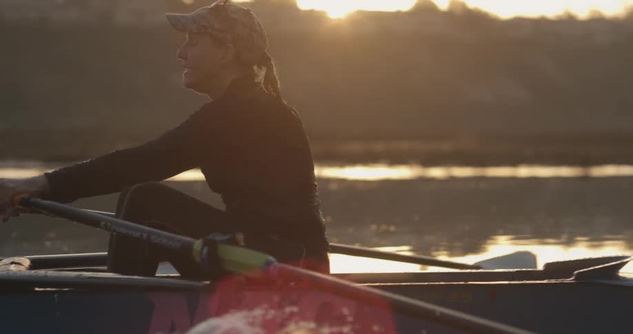 Woman paddling on a rowboat over the calm lake surface at sunset