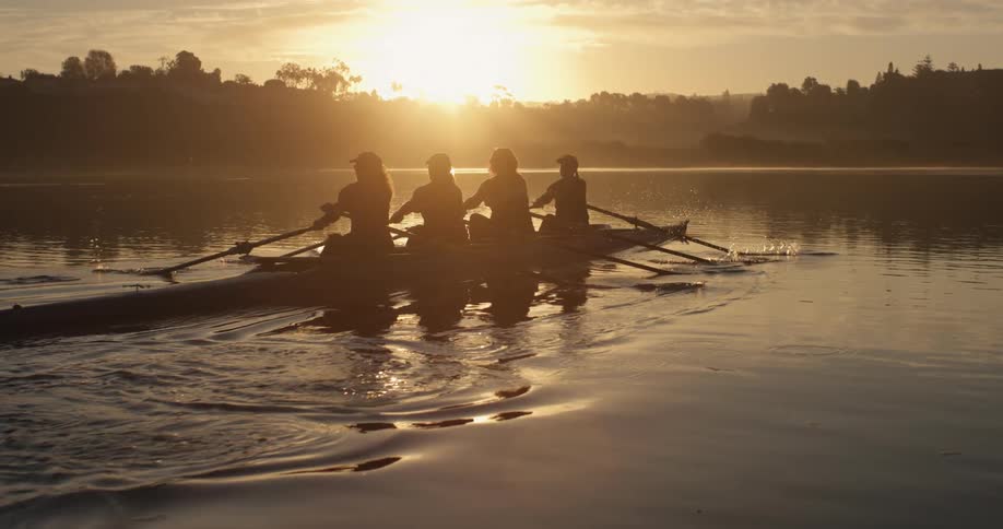 Silhouette of female rowing crew rowing across lake at sunrise