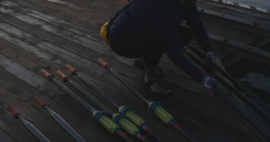 Woman picks up oars from the wooden dock near the lake in front of the city at morning