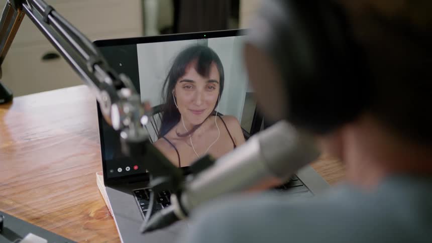 Man wearing a headphone and using a professional microphone to talk to a woman on a video call on a laptop