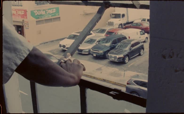A man at home opens his window and looks down at the street as a teenager skateboards by