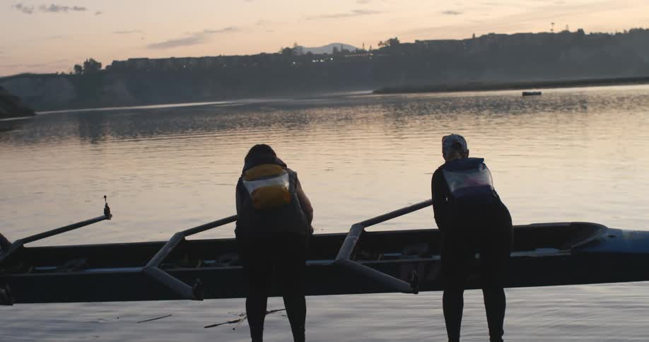Four women hold a boat over their heads and lower it in to the water