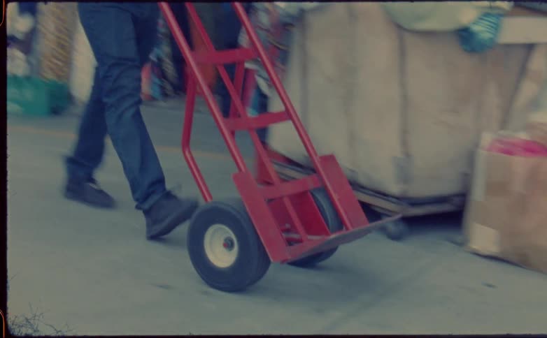 Man wheels hand truck past fabric storefront