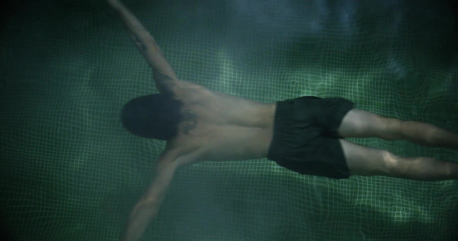 Man with tattoo and black shorts swims in pool