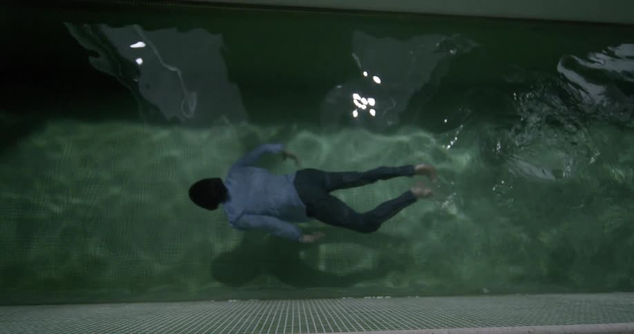 Man wearing blue shirt and pants swimming in an indoor pool