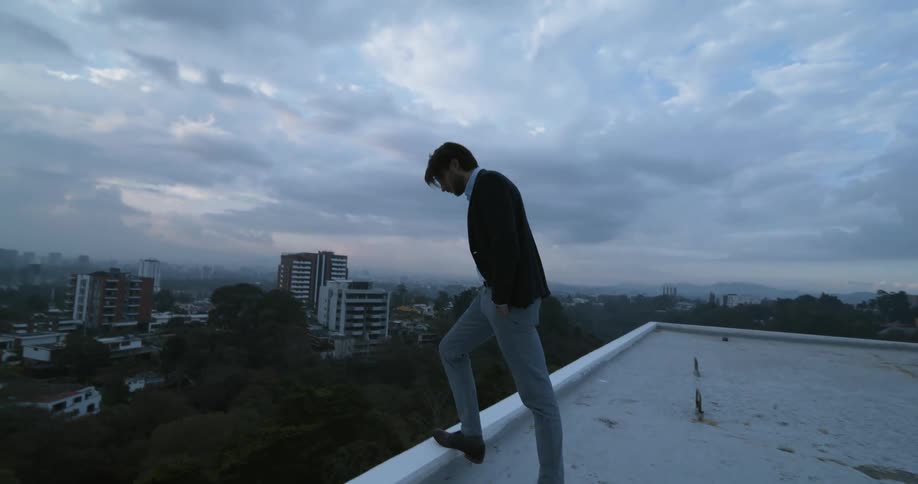Man stepping on ledge on high rise building looking over on a stormy dayd