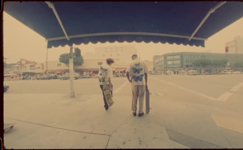 Two people hold skateboards on the sidewalk