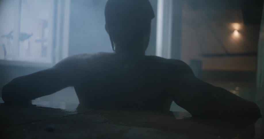 Silhouette of a young man surrounded by steam takes a relaxing bath on a dimly lit hot sauna
