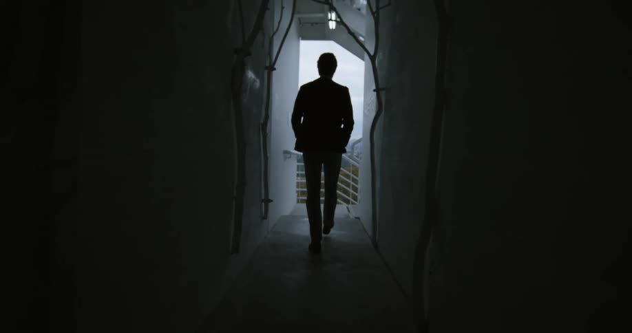 Silhouette of a young man walking out of the dark hallway of a building